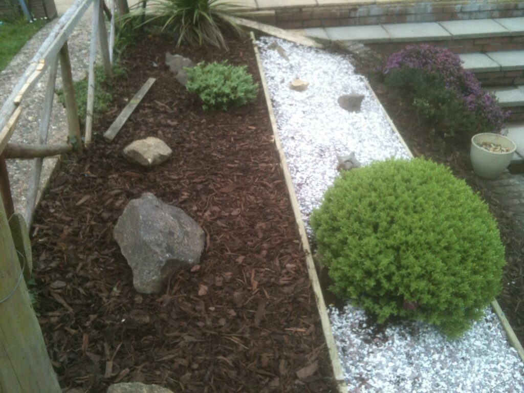 Decorative garden borders with bark mulch, white gravel, timber edging and ornamental shrubs.