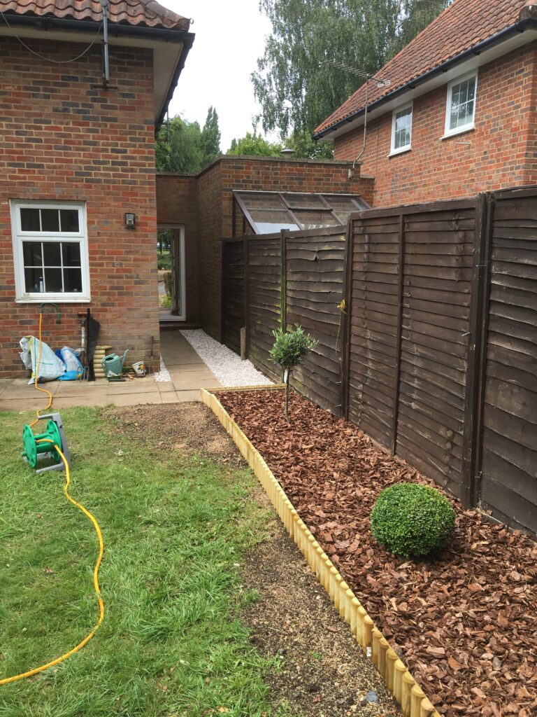 New timber-edged bark border with decorative shrubs installed alongside a garden fence.