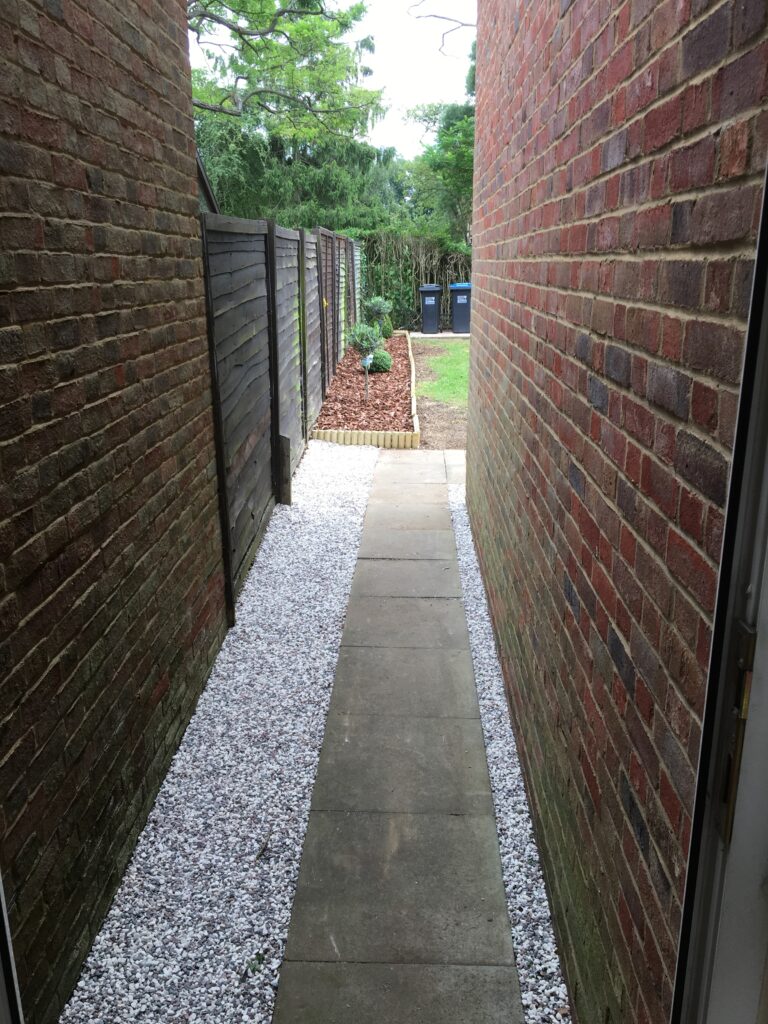 Decorative white gravel installed alongside a narrow side path to improve drainage and reduce maintenance.